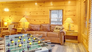 Una habitación acogedora con mesa de fútbol, sofá de cuero, paredes de madera y dos lámparas.