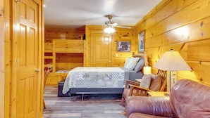Una habitación de cabaña de madera con una cama, una silla, una mesa y un ventilador de techo.