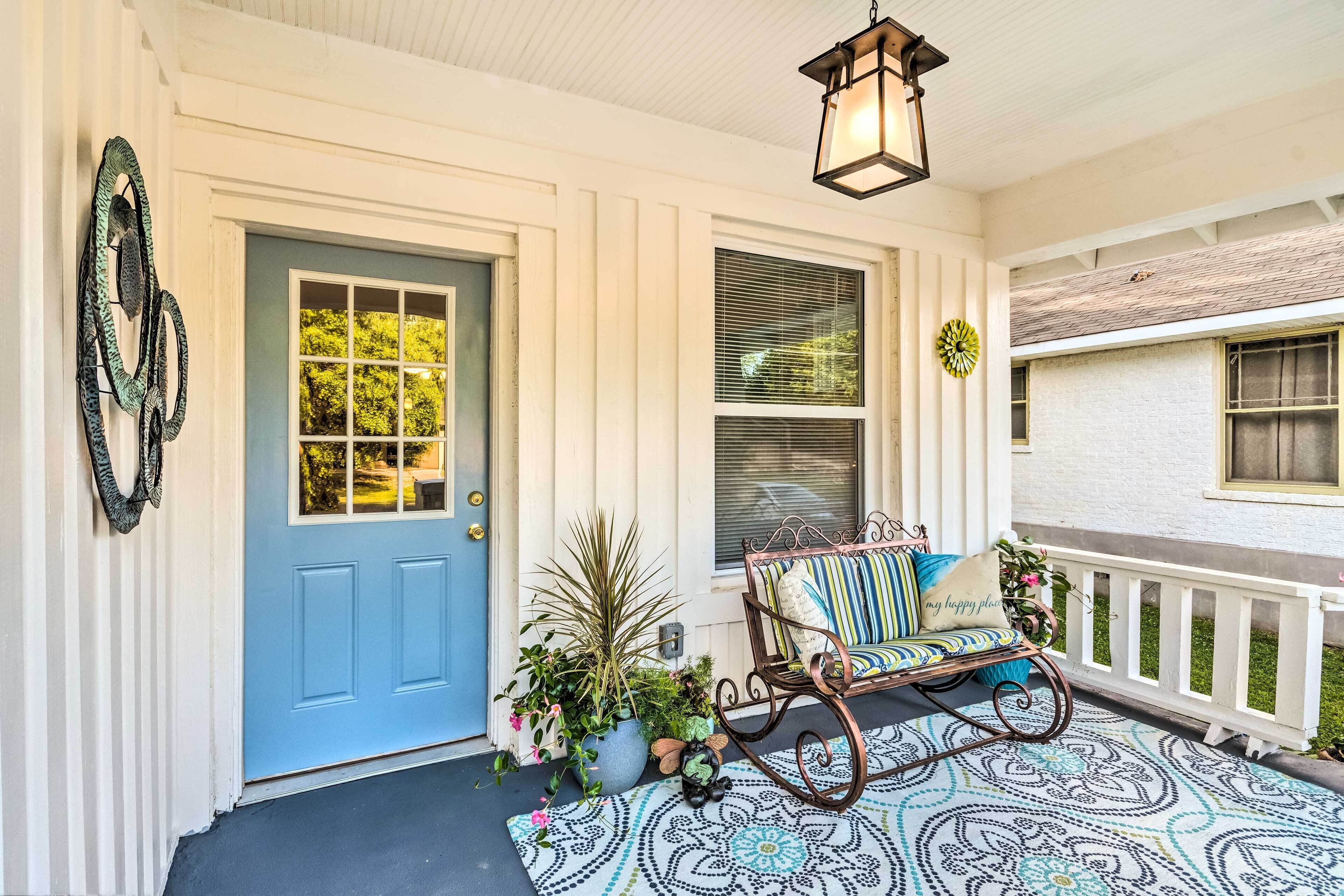 Une véranda avec une porte bleue, une chaise berçante et des plantes en pot.
