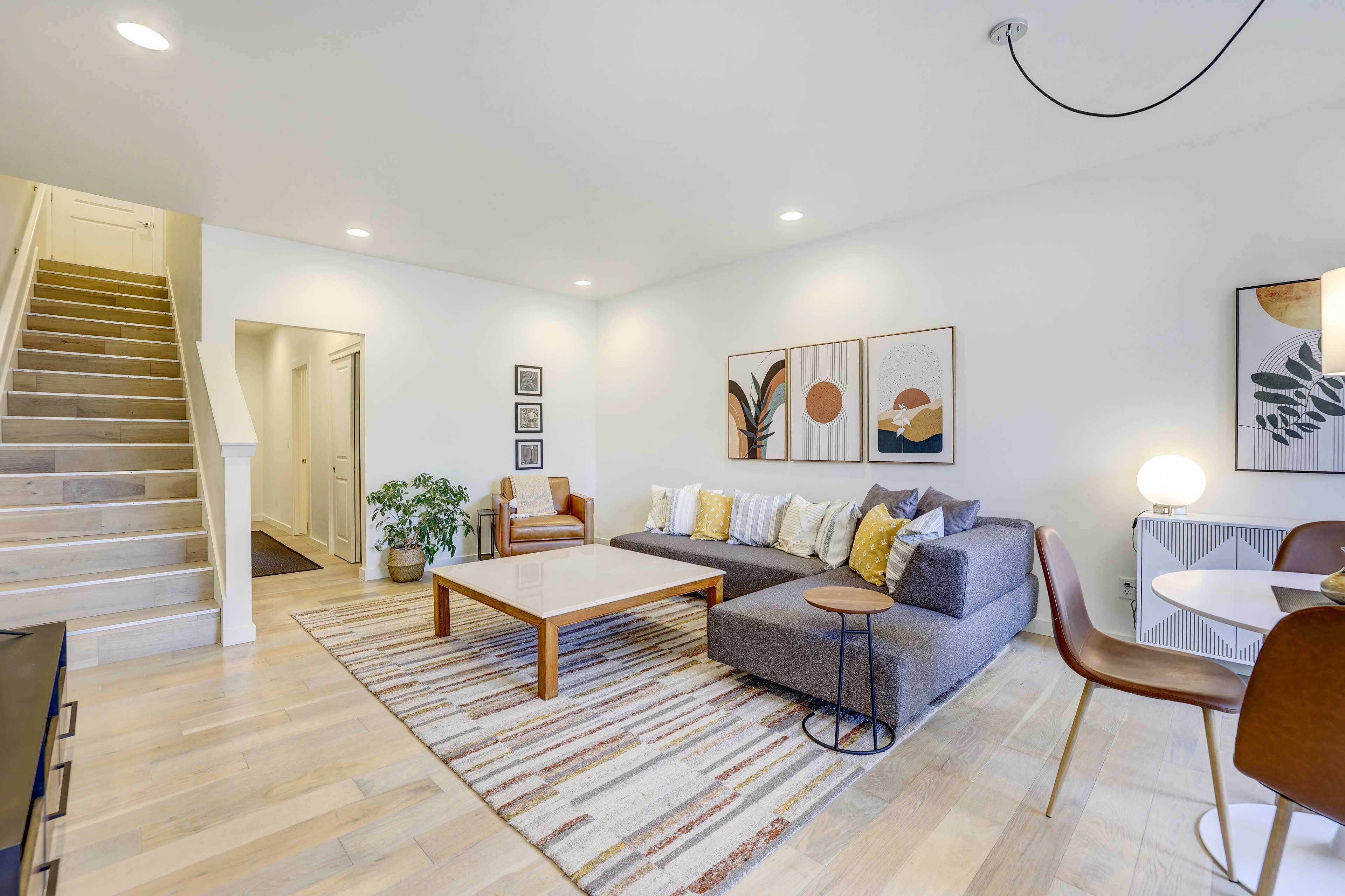 Ein modernes Wohnzimmer mit Treppe, grauem Sofa, Couchtisch und Essbereich mit Tisch und Stühlen.