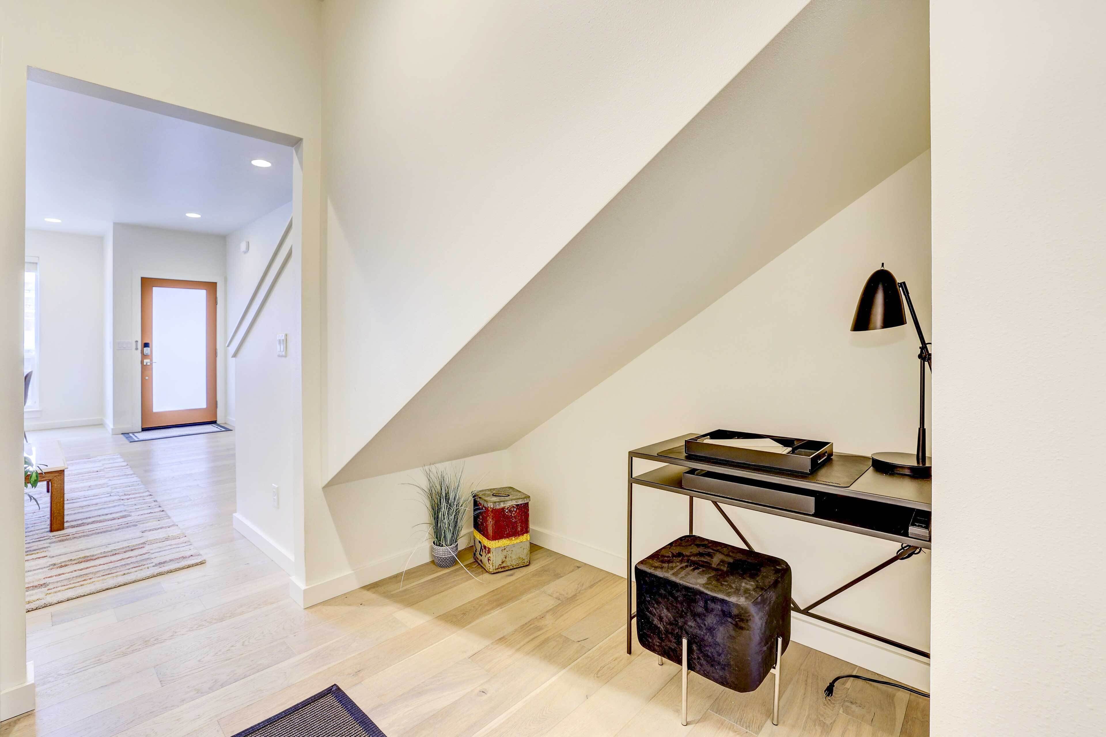 A modern loft bedroom with a sloped ceiling, a desk with a lamp, and a small ottoman.