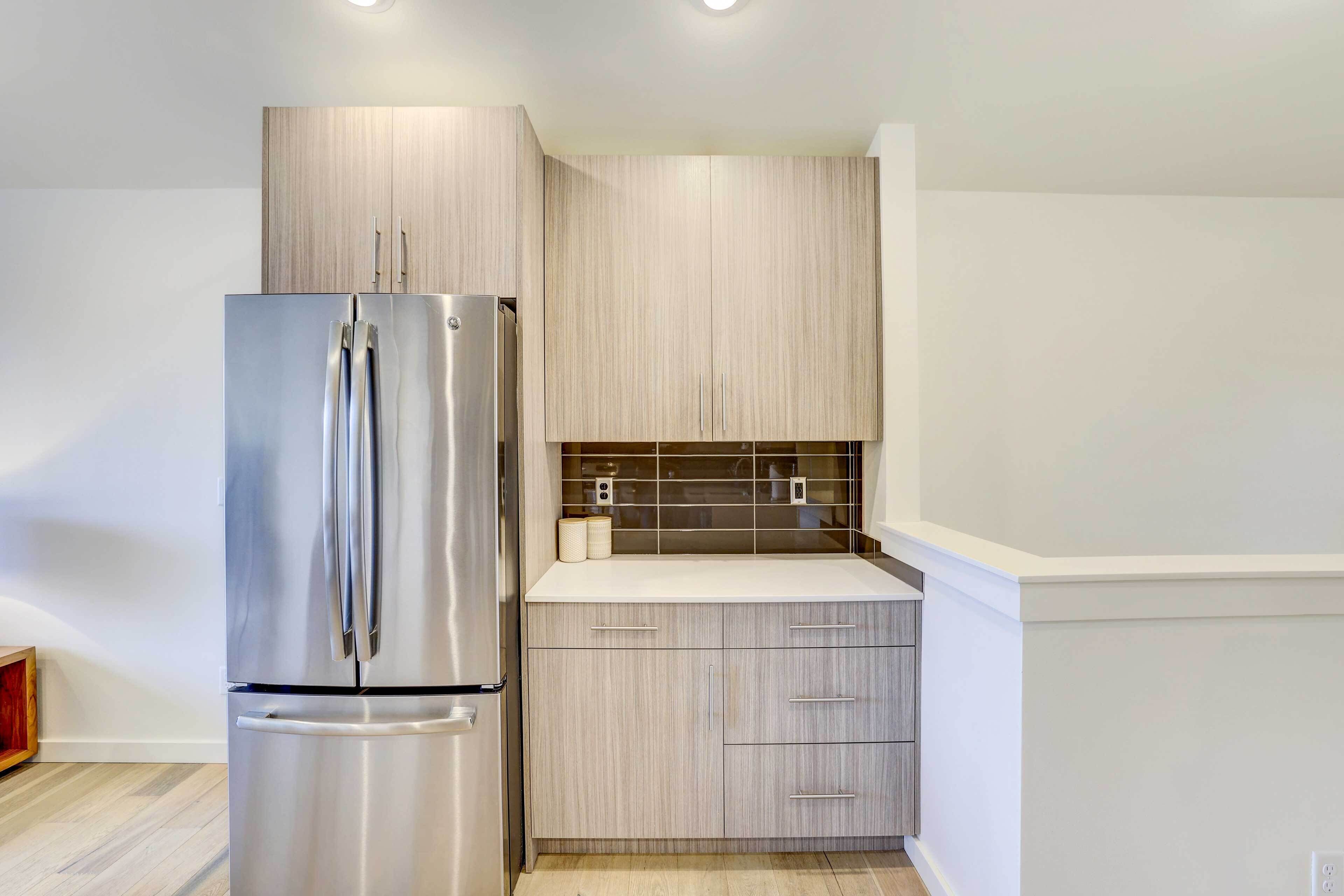 Una cocina moderna con refrigerador de acero inoxidable, armarios de madera y encimera blanca.