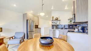 A modern kitchen with stainless steel appliances, a dining area with a wooden table and chairs, and a light fixture above the table. - Beautiful Townhome - Steps to Downtown Boise! (Boise)