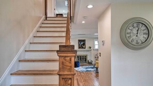 A staircase with wooden steps and a wooden handrail, leading to a room with a fireplace and a clock on the wall. - Charming Cape Charles Vacation Rental Home! (Cheriton)