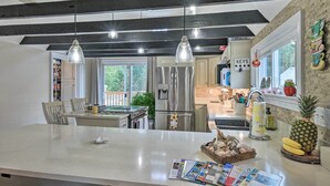 A modern kitchen with a central island, stainless steel appliances, pendant lighting, and a view of the outdoors. - Charming Cape Charles Vacation Rental Home! (Cheriton)
