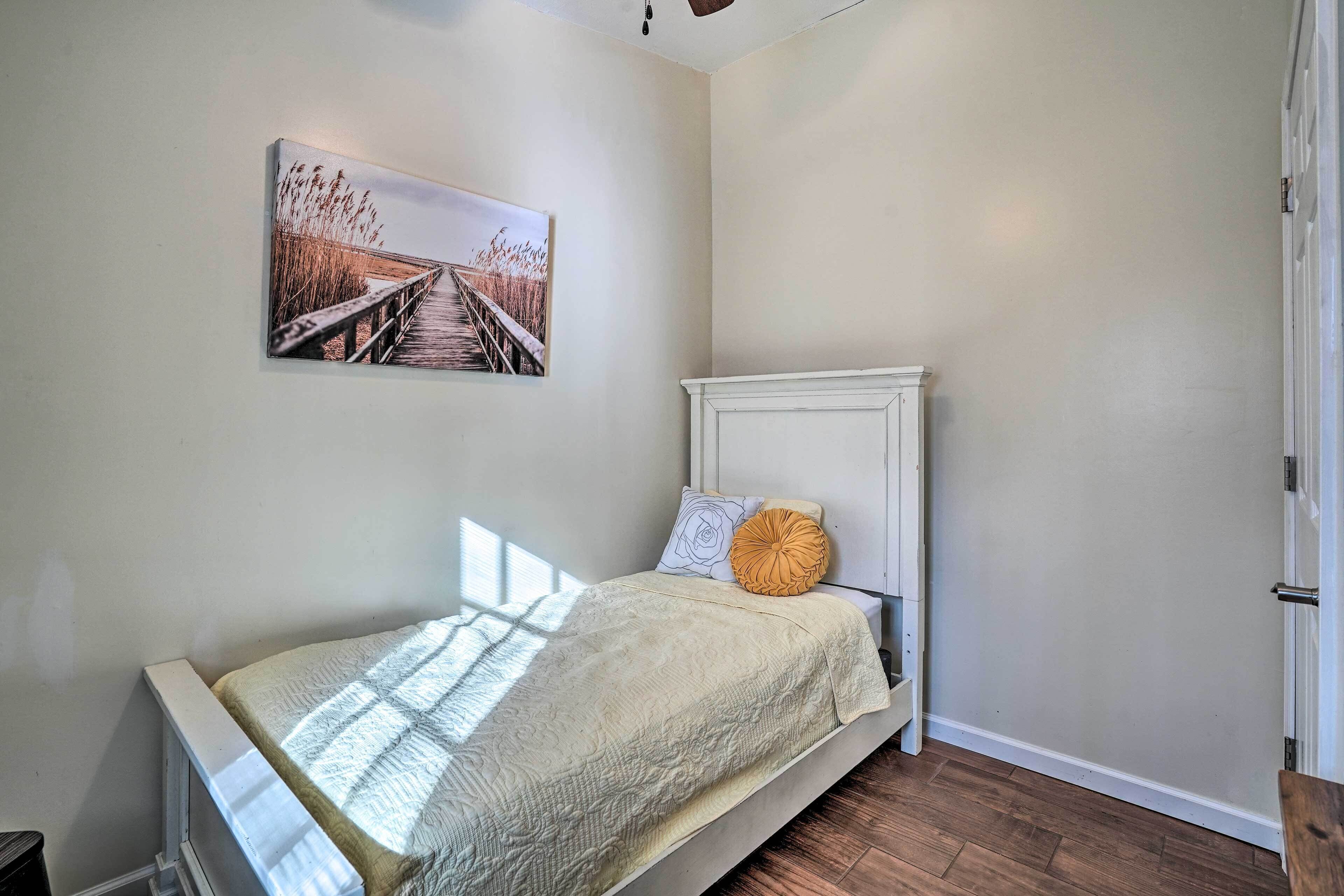 A bedroom with a bed, a white headboard, a window, and a painting on the wall.