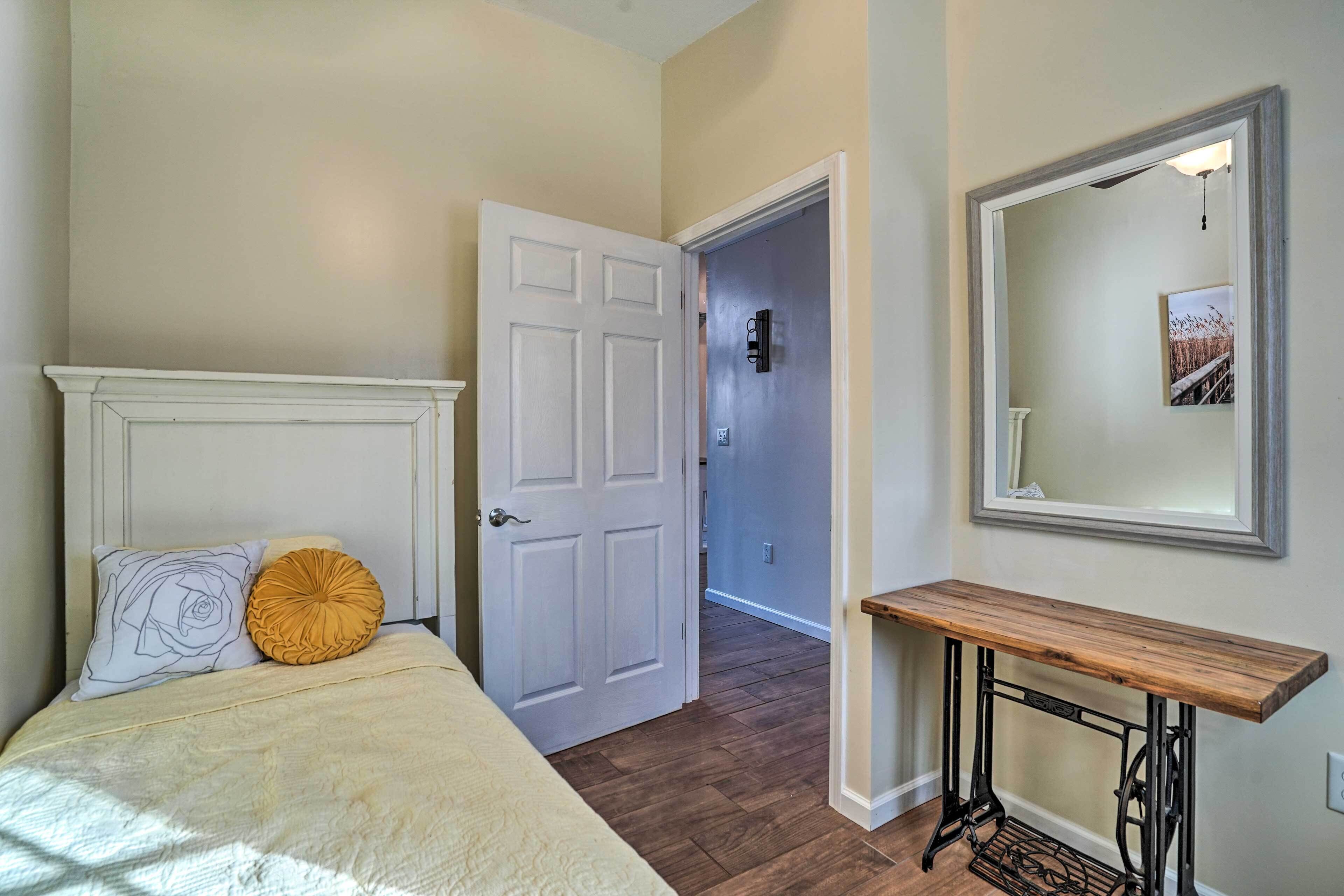 Un dormitorio con cama, mesita de noche, espejo y una puerta que da a otra habitación.