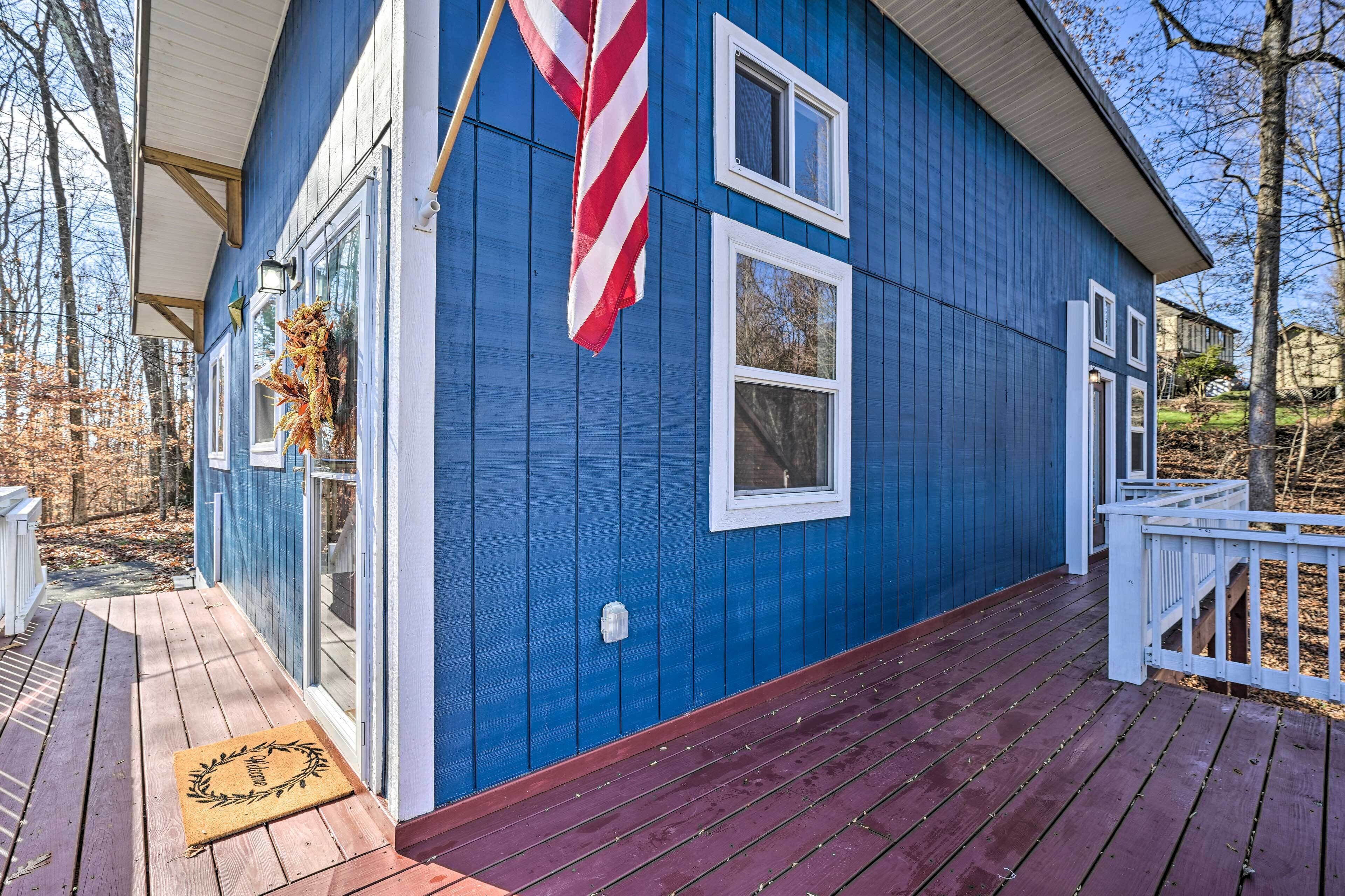 A blue house with a porch, a red and white striped flag, and a wreath on the door.