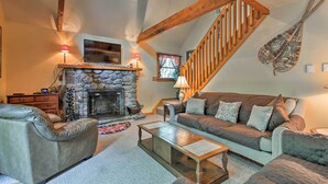 Ein gemütliches Wohnzimmer mit Kamin aus Stein, Ledersofas, einer Holztreppe und einer an der Wand befestigten Geige.