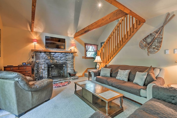 A cozy living room with a stone fireplace, leather sofas, a wooden staircase, and a mounted violin.