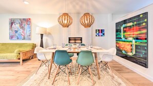A modern dining area with a white table, teal chairs, and wooden chairs. There is a green sofa, a lamp, and a painting on the wall. - Modern Jacksonville Beach Retreat w/ Hot Tub! (Jacksonville Beach)