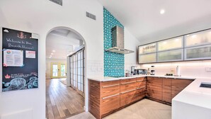 A modern kitchen with wooden cabinets, a white countertop, and a teal backsplash. - Modern Jacksonville Beach Retreat w/ Hot Tub! (Jacksonville Beach)