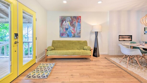 A room with a green sofa, a dining table with chairs, a painting on the wall, and a yellow door. - Modern Jacksonville Beach Retreat w/ Hot Tub! (Jacksonville Beach)