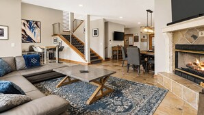 A modern living room with a sofa, coffee table, fireplace, and a staircase leading to a dining area. - Hot Tub, 2 Mi to Cabriolet Lift: Family Mtn Escape (Park City)