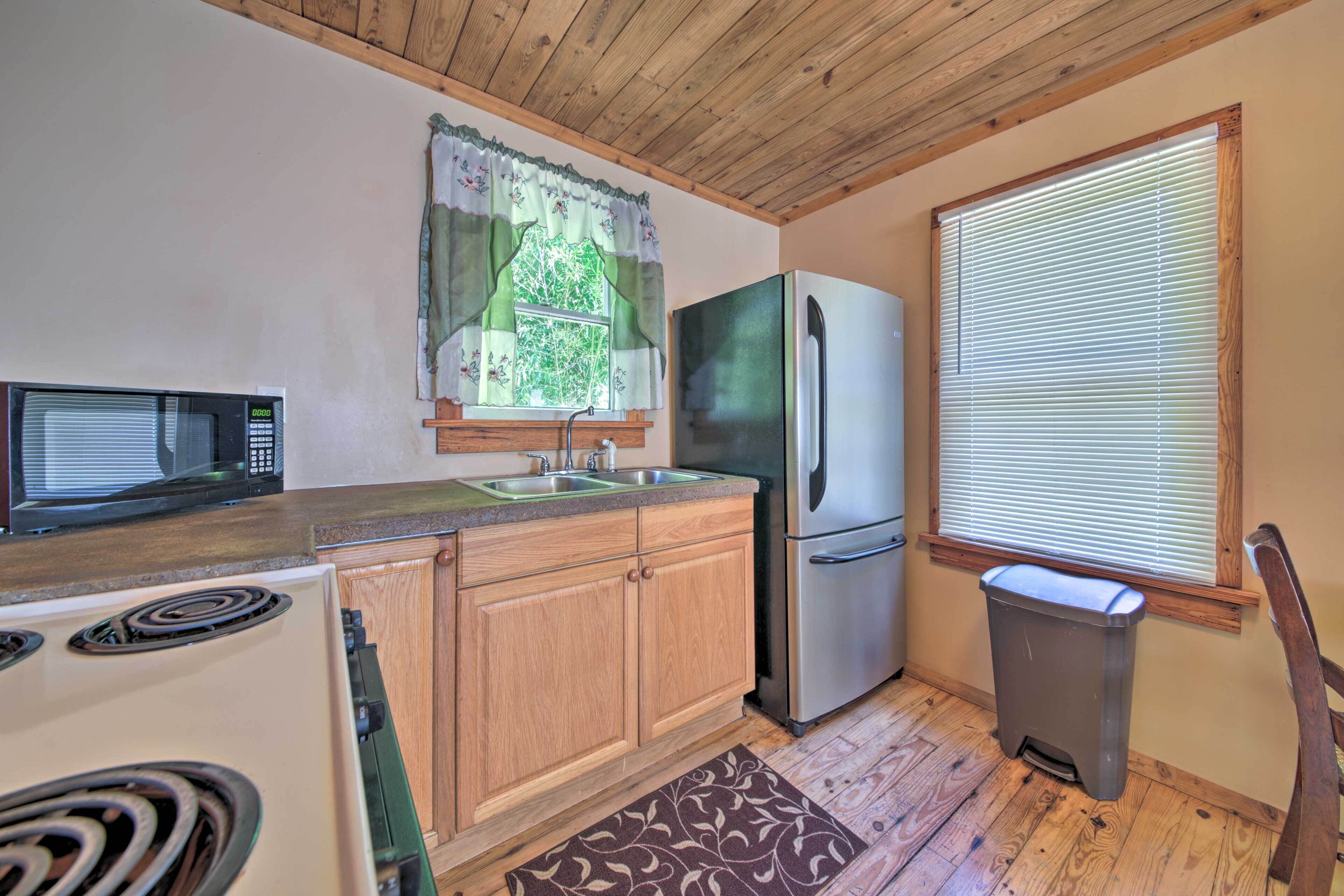 A compact kitchen with wooden cabinets, a microwave, a refrigerator, and a trash can.