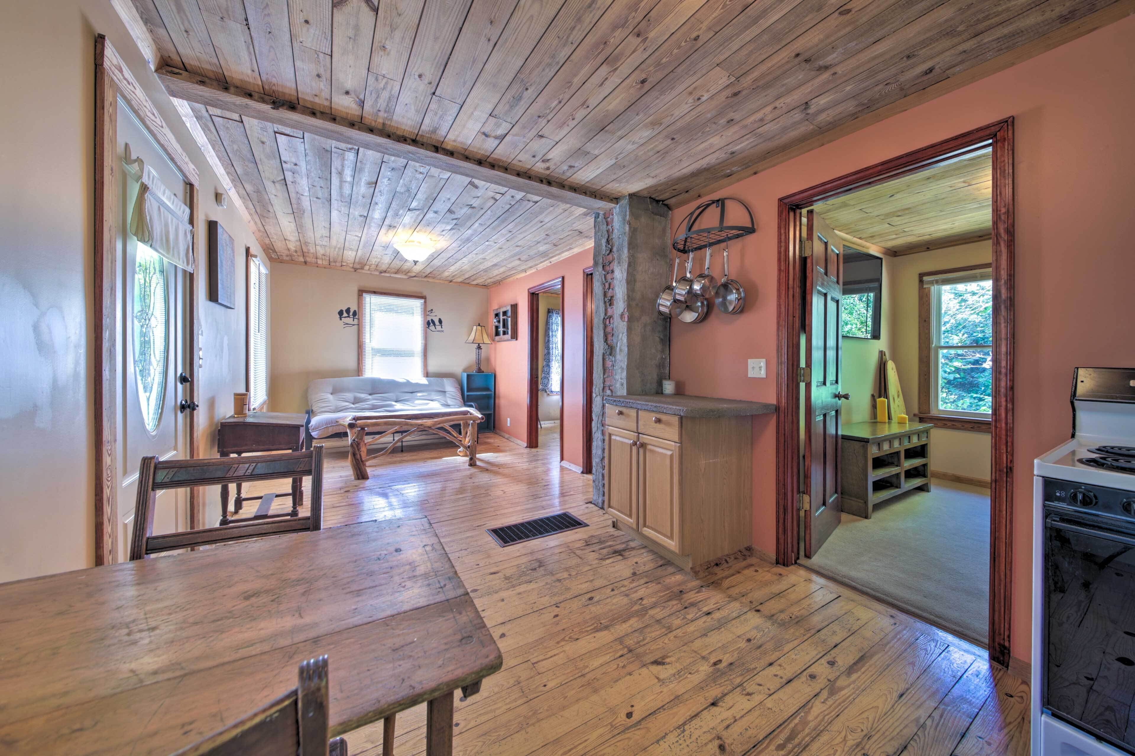 A rustic interior with a wooden dining table, a bed, and a kitchen area with a stove.