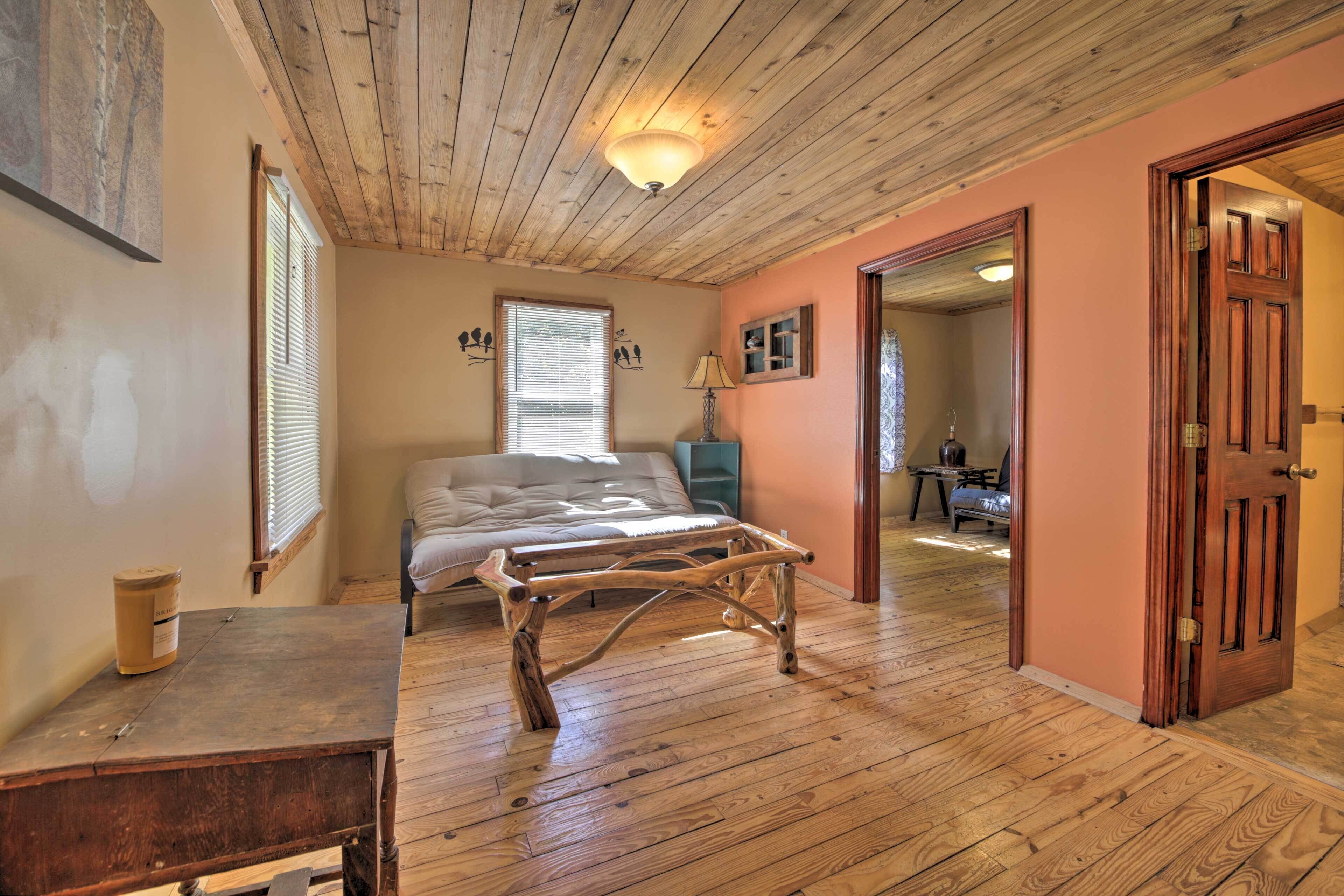 A bedroom with a wooden ceiling, a bed, a wooden table, and a door leading to another room.