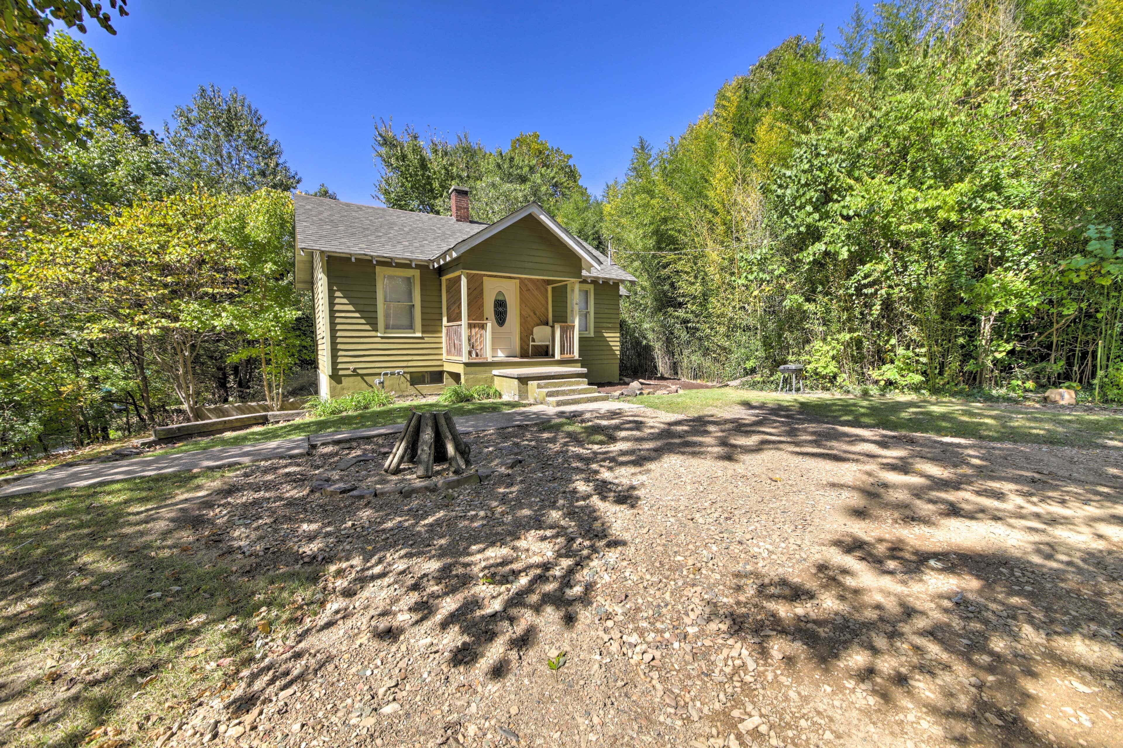 A two-story house with a porch, surrounded by trees and a gravel driveway.
