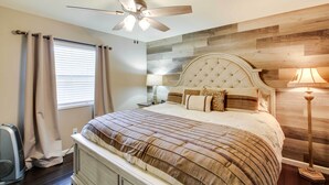 A bedroom with a tufted headboard, a bed with a striped bedspread, a ceiling fan, a bedside lamp, and a window with curtains. - Lakefront Haven Near Oaklawn & Casino Resort! (Hot Springs)