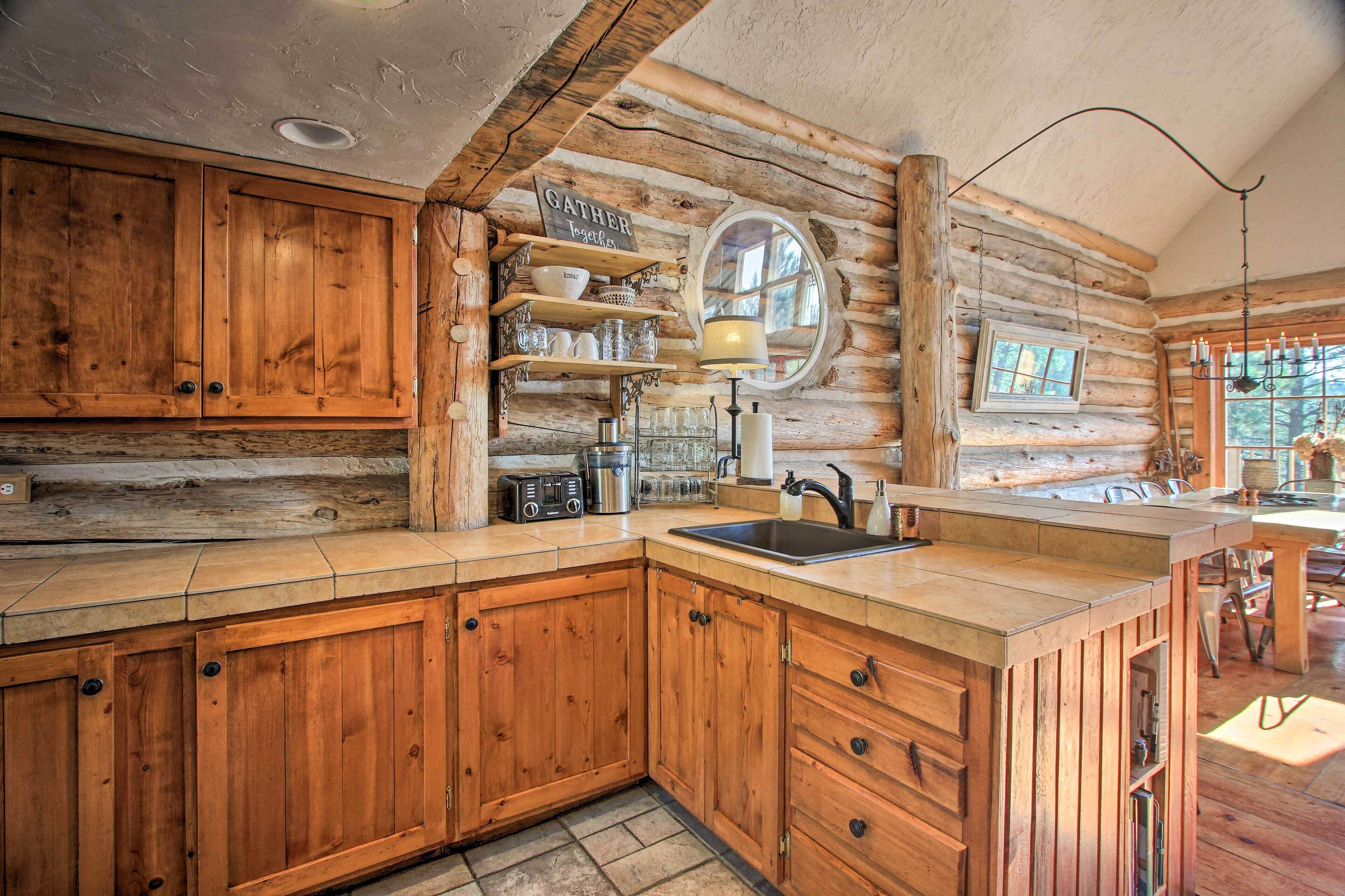 A rustic kitchen with wooden cabinets, a built-in sink, and a window overlooking a forest.