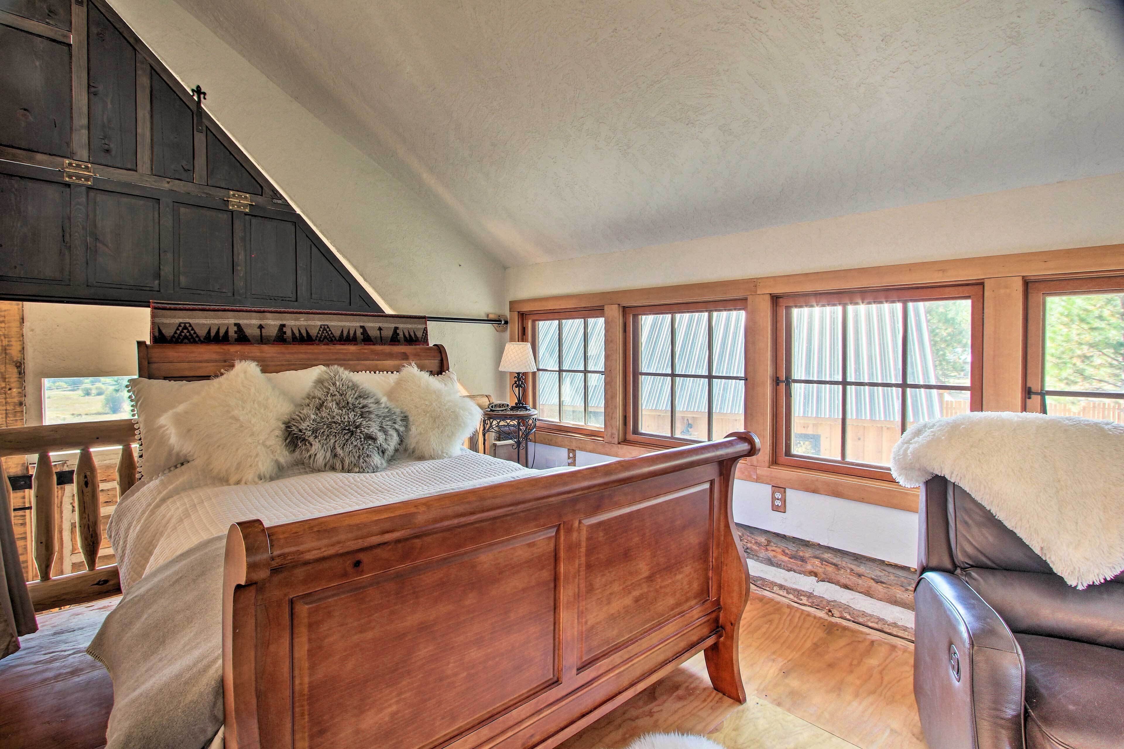 A bedroom with a wooden bed, a chair, and large windows.