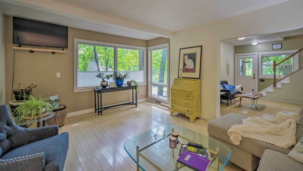 A spacious living room with a glass coffee table, a sofa, a television mounted on the wall, and a staircase leading to another level.