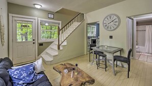 A living room with a staircase, a dining area with a table and chairs, and a clock on the wall.