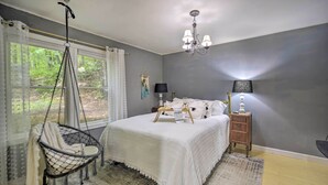 A bedroom with a bed, a hanging chair, a bedside table with a lamp, and a window with curtains.