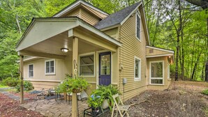 A two-story house with a covered porch, a front door, and a small garden area with potted plants and a chair.