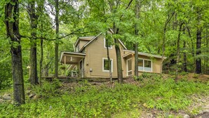 A cabin in a forest with a porch and a small deck.
