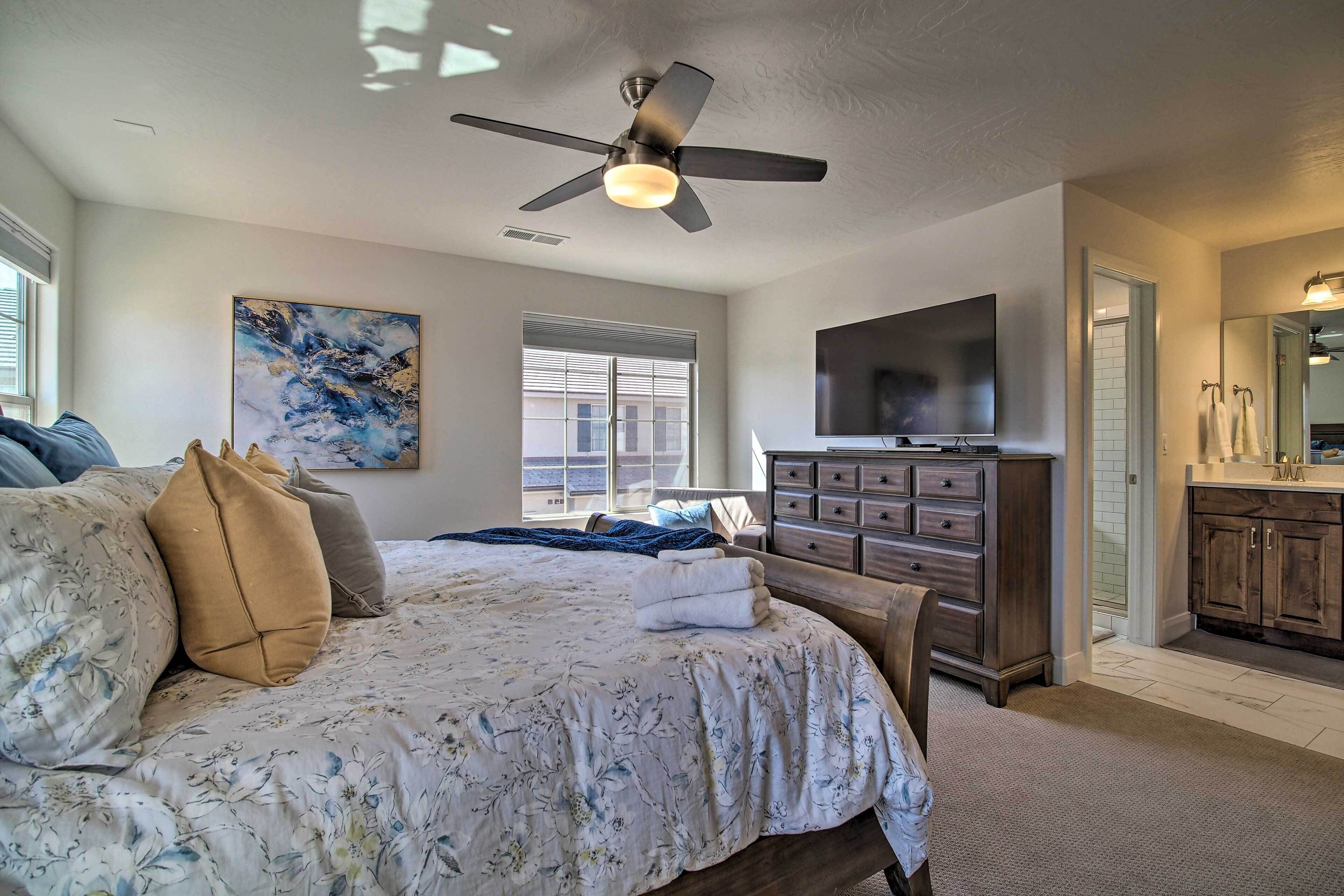 A bedroom with a bed, a ceiling fan, a TV, a dresser, and a window.
