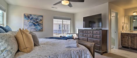 A bedroom with a bed, a ceiling fan, a TV, a dresser, and a window.