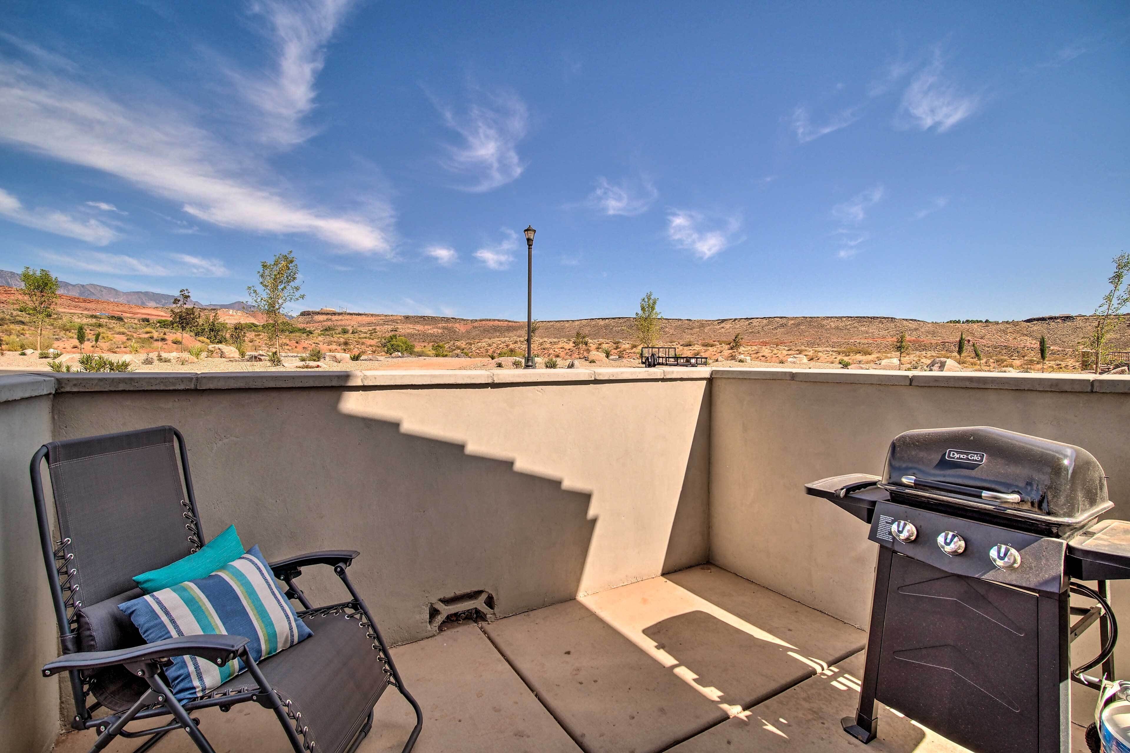 Eine Terrassenanlage im Freien mit Grill, Stuhl mit Kissen und Blick auf eine Wüstenlandschaft.