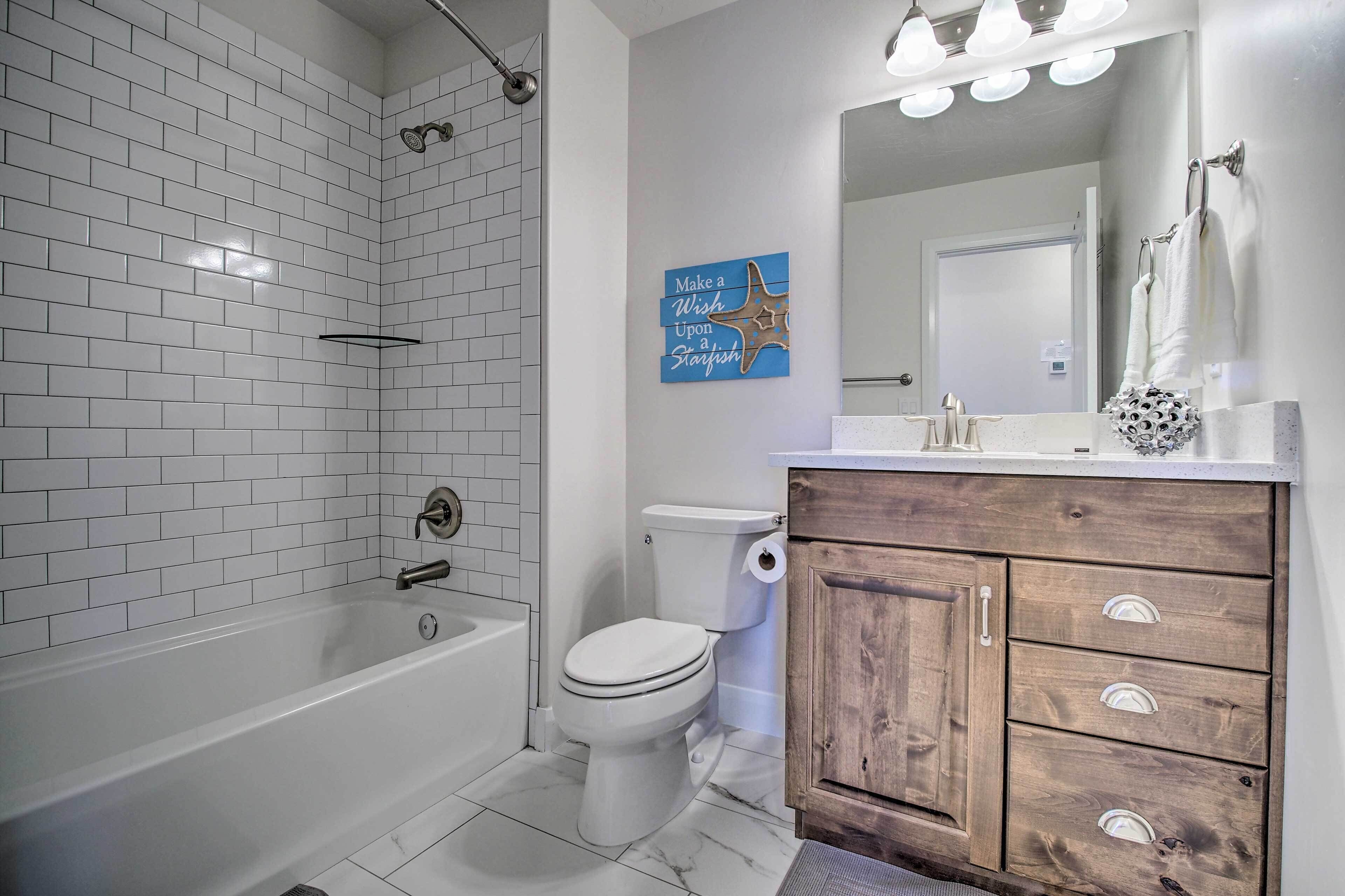 A modern bathroom with white subway tiles, a white bathtub, a toilet, and a wooden vanity with drawers.