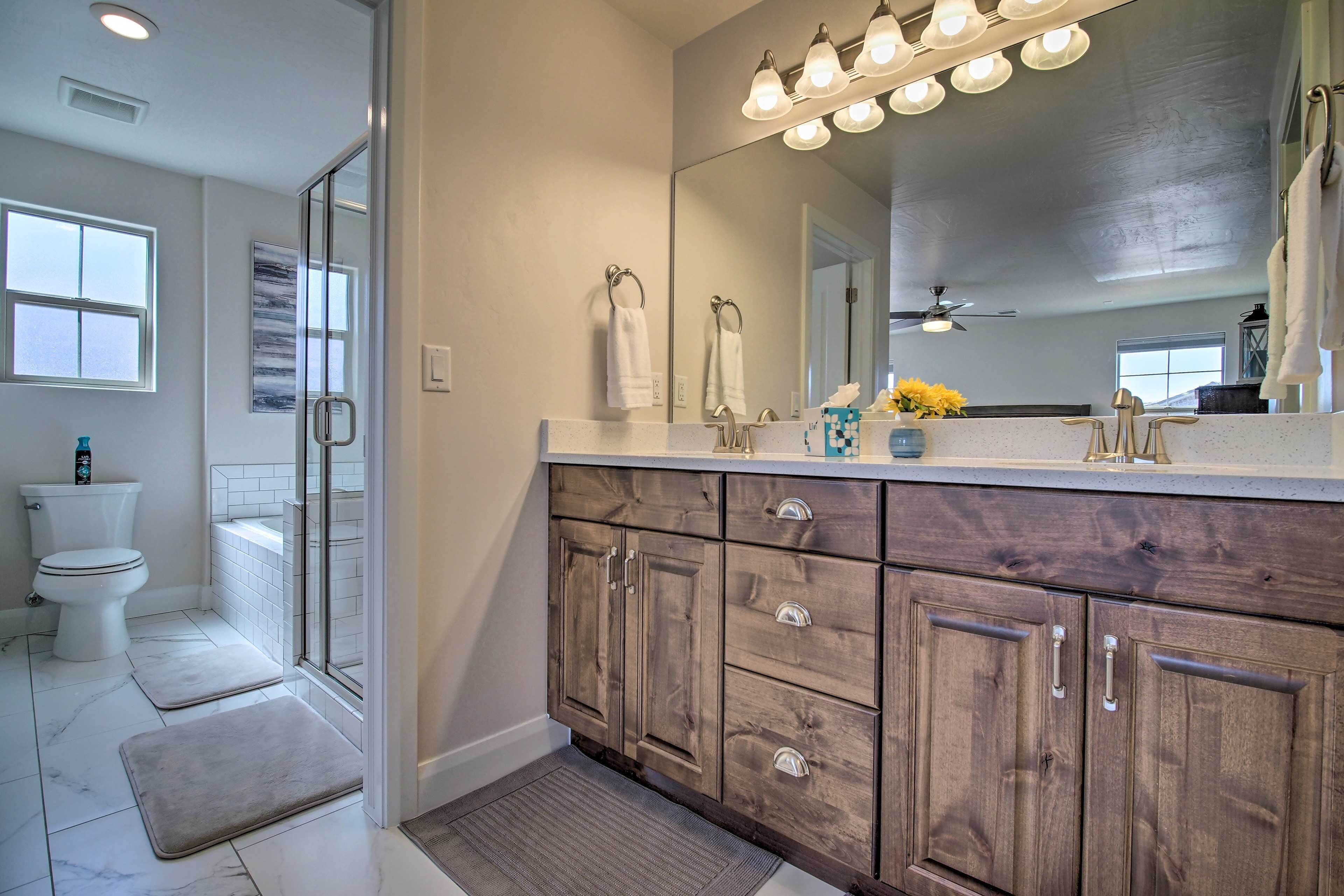 A bathroom with a shower, toilet, and vanity with a mirror and lights.
