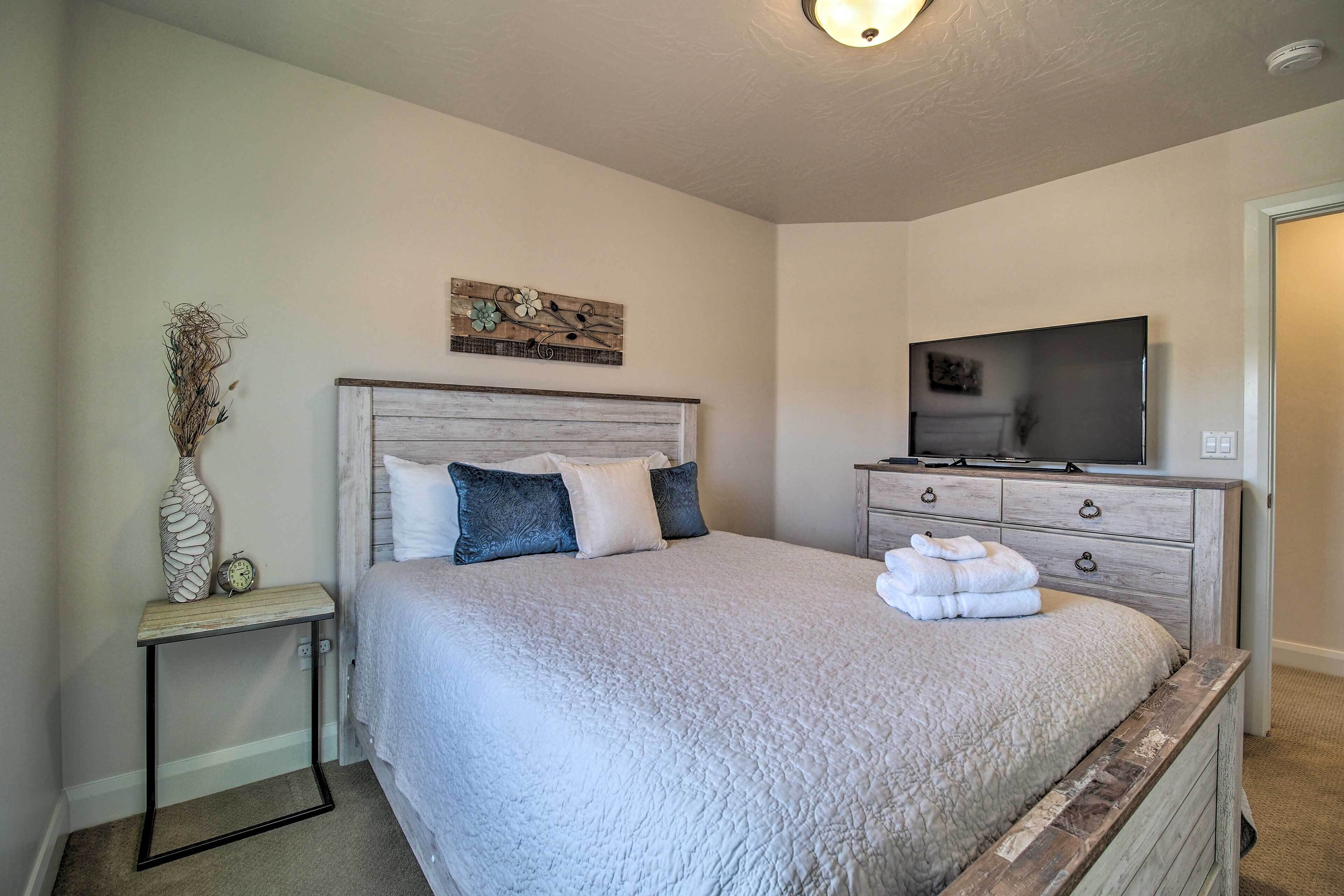 Une chambre à coucher avec un lit, une télévision, une commode et une petite table sur laquelle se trouvent un vase et une horloge.