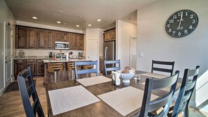 A modern kitchen with wooden cabinets, stainless steel appliances, and a dining area with a large clock on the wall. - Modern Washington Home - Pool & Trail Access! (Washington)