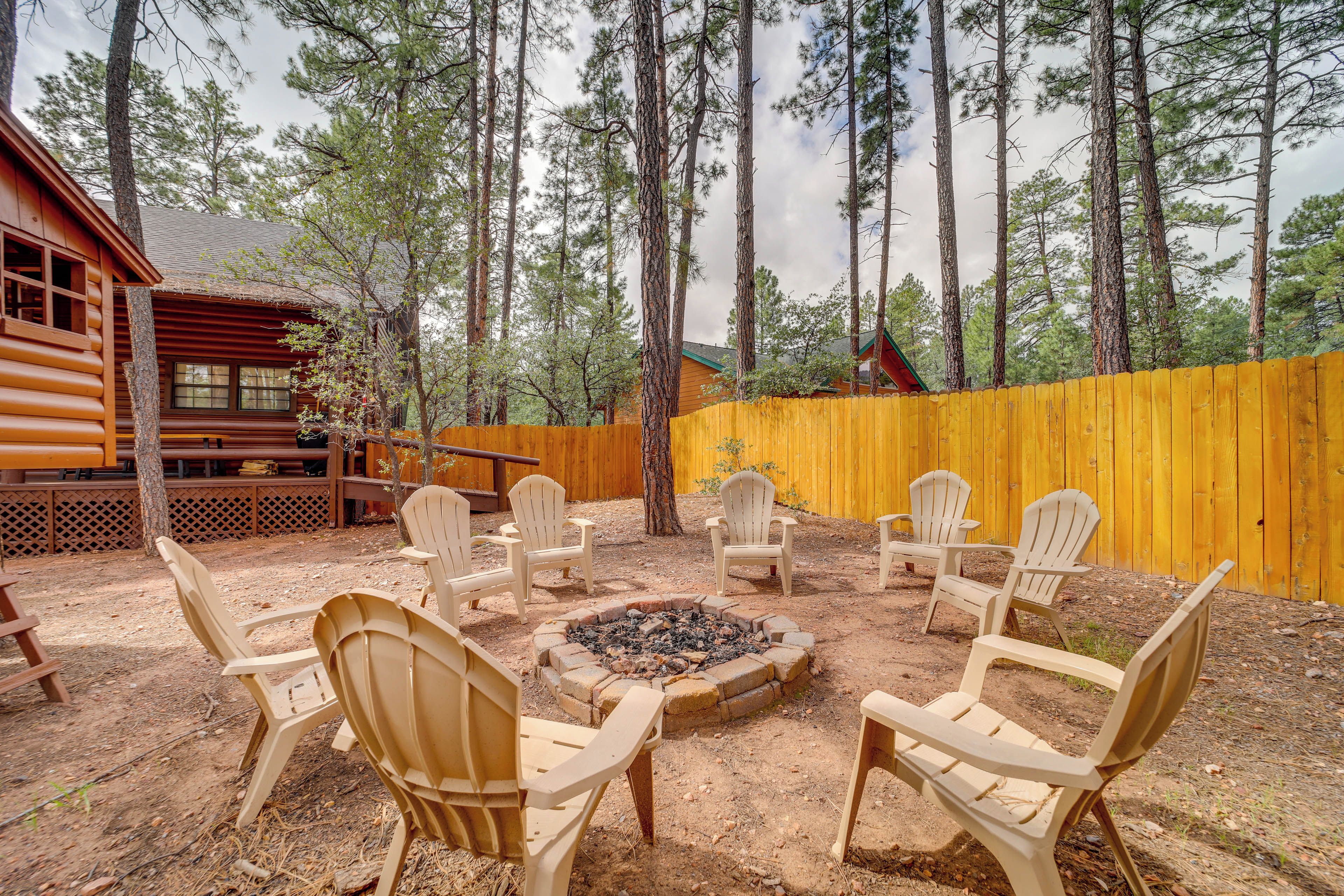 Una cabaña de madera con terraza, rodeada por una cerca amarilla y altos pinos.
