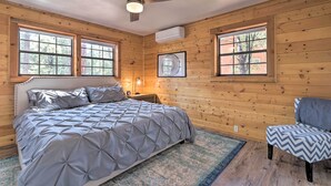 A bedroom with a bed, a chair, a ceiling fan, and large windows. - Deck, Games & Fire Pit: Modern Pine Cabin! (Pine)