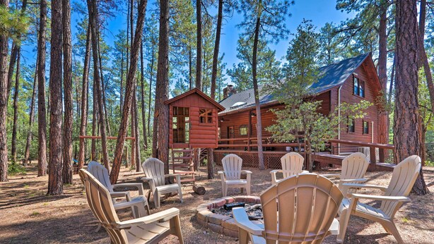 A cabin with a deck, surrounded by tall pine trees. There are Adirondack chairs arranged around a fire pit. - Deck, Games & Fire Pit: Modern Pine Cabin! (Pine)