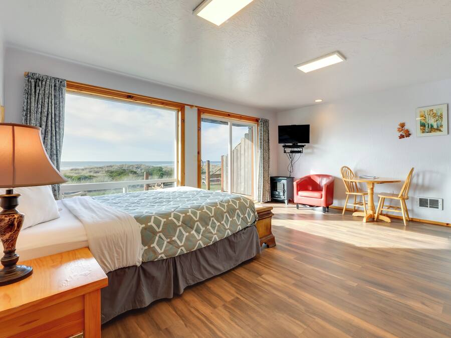 A bedroom with a bed, a desk, and a chair, a television, and a large window with a view.