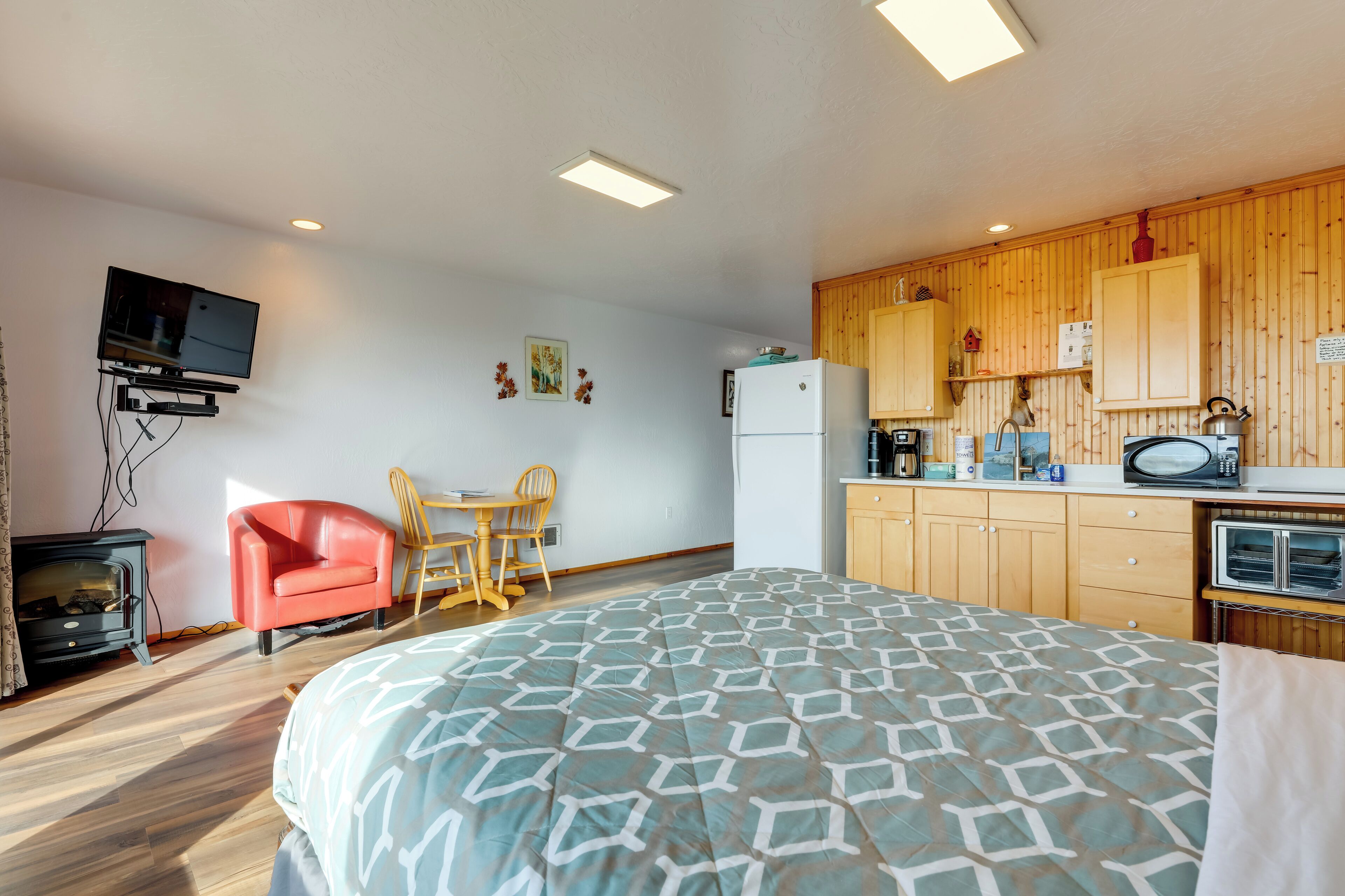 Ein kompaktes Hotelzimmer mit Bett, einer kleinen Küchenzeile, einem an der Wand befestigten Fernseher und einem Essbereich aus Holz.