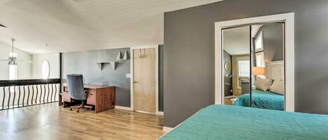 A modern bedroom with a wooden floor, a desk, a chair, a bed with a teal bedspread, and a large mirror.