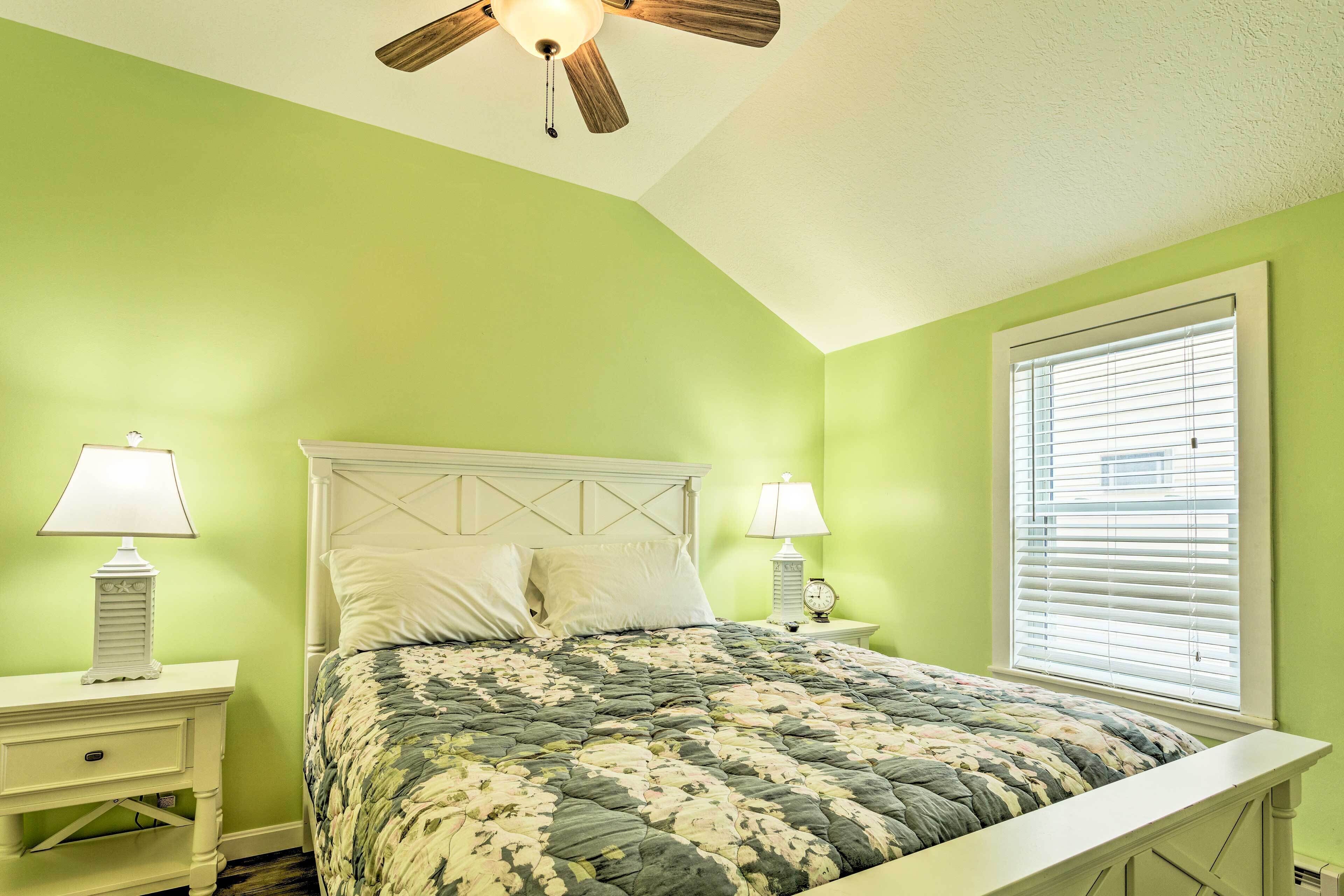 A bedroom with a bed, two bedside tables with lamps, a ceiling fan, and a window with blinds.
