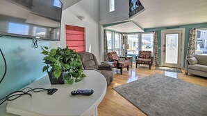 A spacious living room with a flat-screen TV, a potted plant, a sofa, and a dining area with chairs. - Sun-soaked Coastal Cottage w/ Deck + Walk to Beach (Old Orchard Beach)