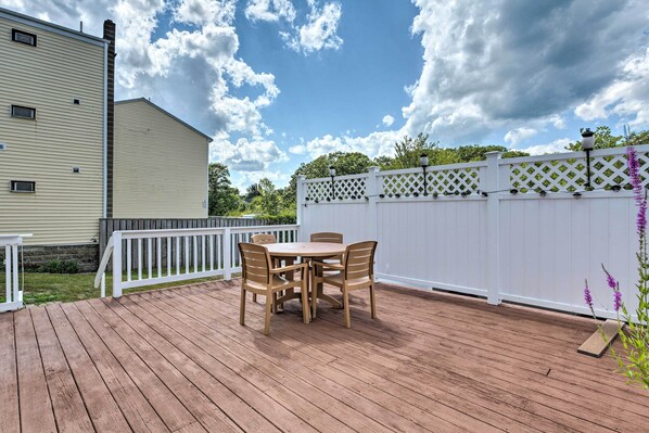 A wooden deck with a table and chairs, a white fence, and a building in the background.