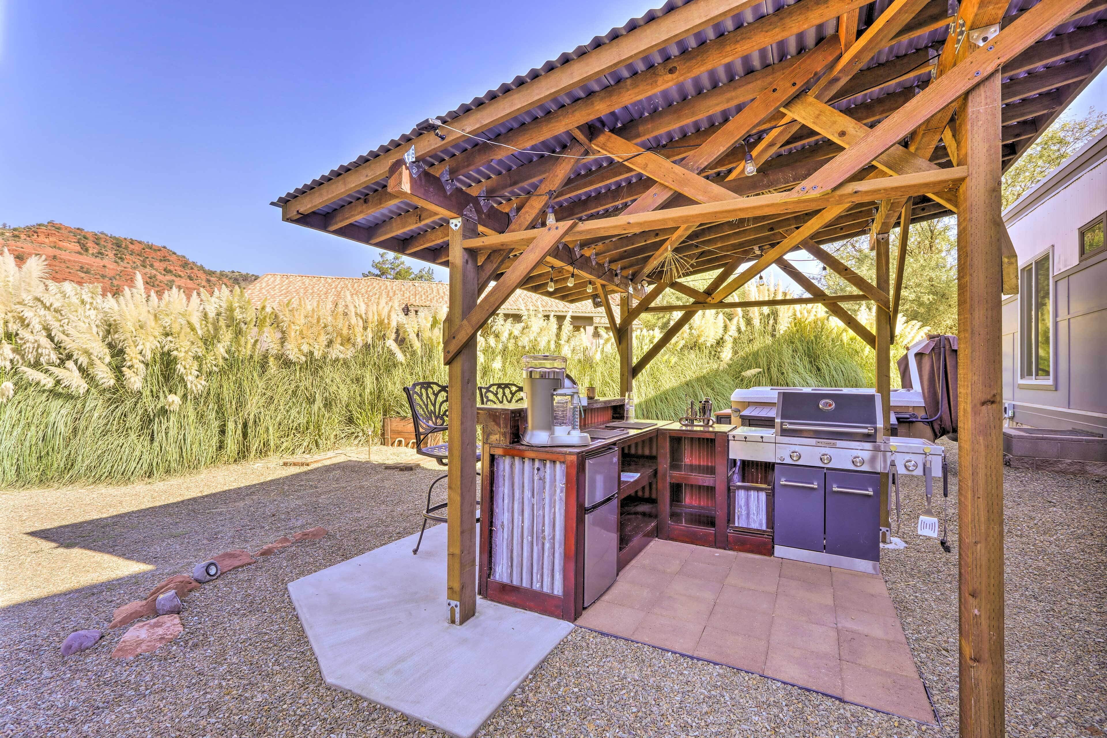 An outdoor patio with a wooden pergola, a grill, and a refrigerator.