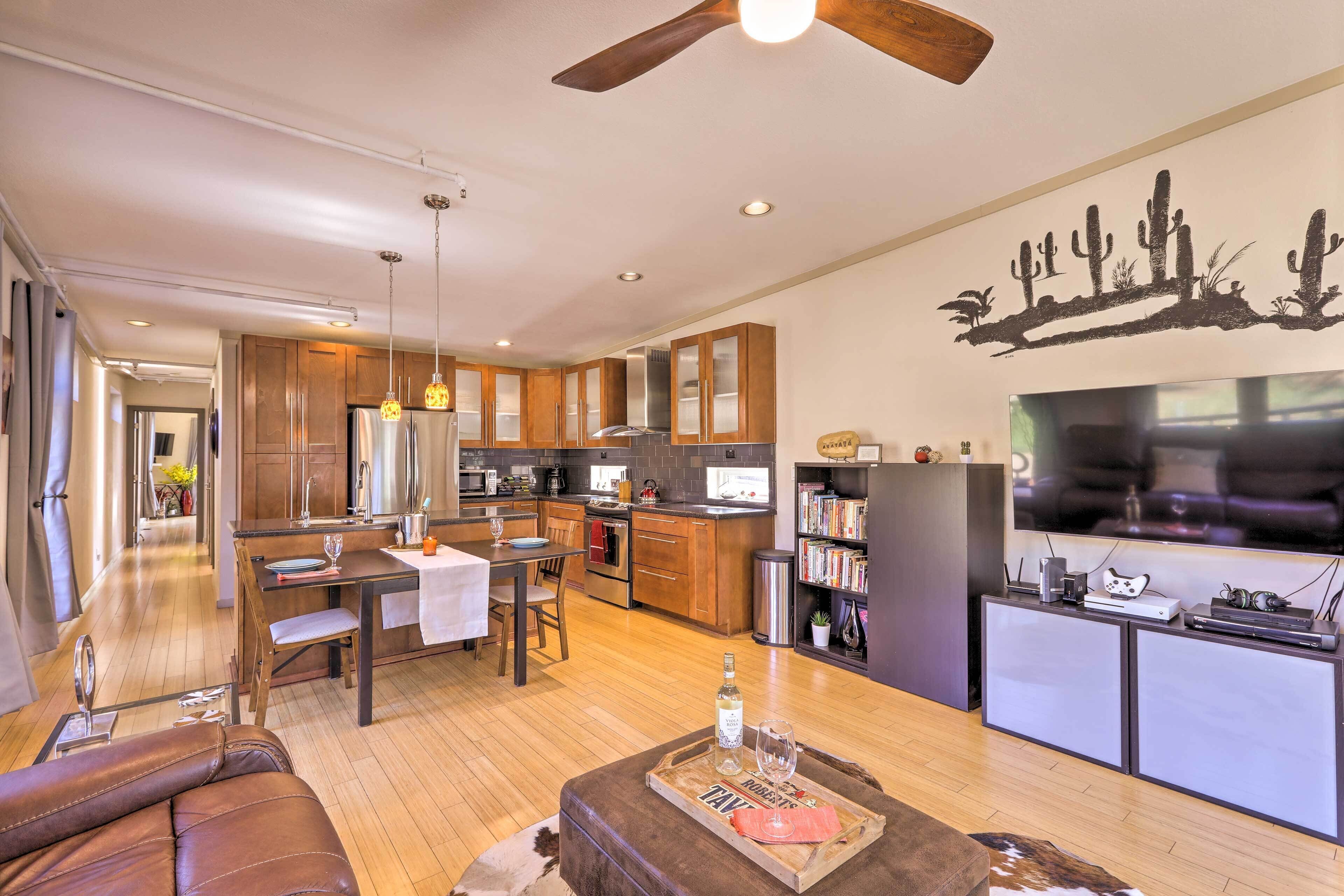 A modern kitchen with wooden cabinets, a dining area with a table and chairs, and a living room with a leather couch and a coffee table.