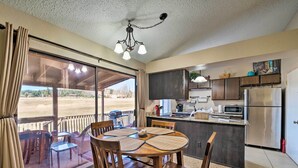A dining area with a table and chairs, a kitchen with modern appliances, and a large sliding glass door leading to an outdoor patio. - Condo on Golf Course: 2 Mi to Grindstone Lake! (Ruidoso)