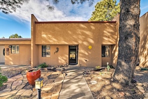 A building with a stone pathway leading to the entrance, a large tree to the right, and a potted plant in the foreground. - Condo on Golf Course: 2 Mi to Grindstone Lake! (Ruidoso)